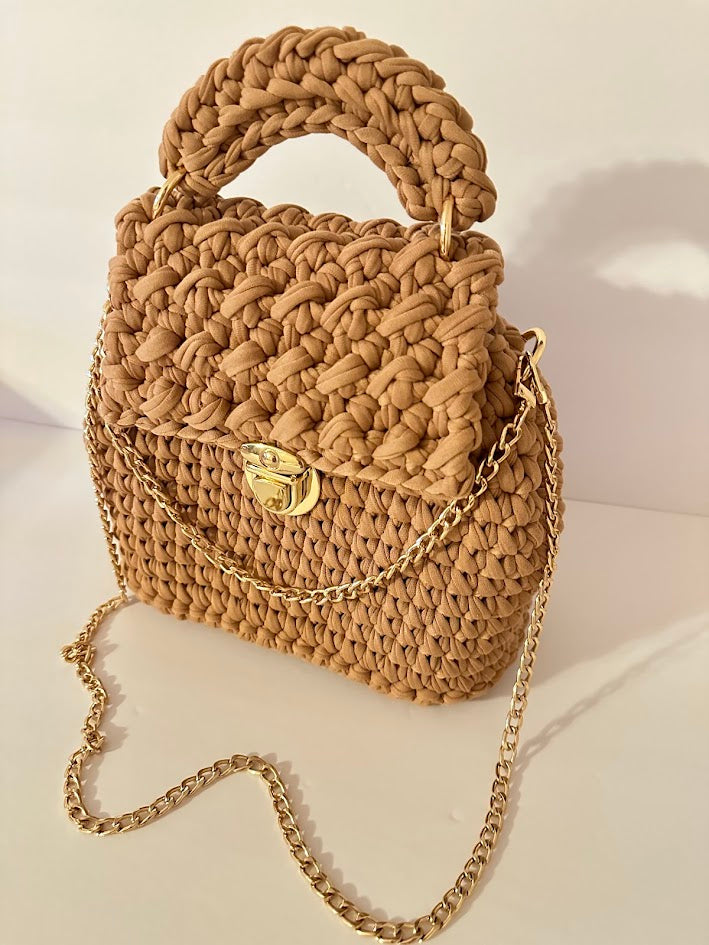 Beige woven handbag with a gold chain on a light background